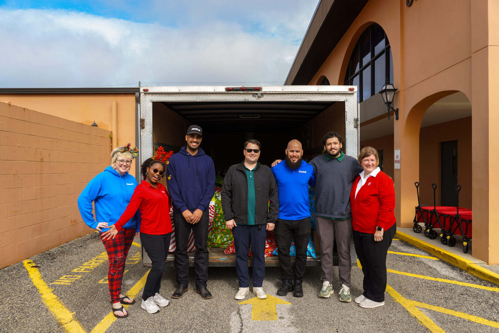 2 Salvation Army staff members with 5 MaintenX employees at the Salvation Army drop-off in front of the MaintenX trailer with all the gifts.